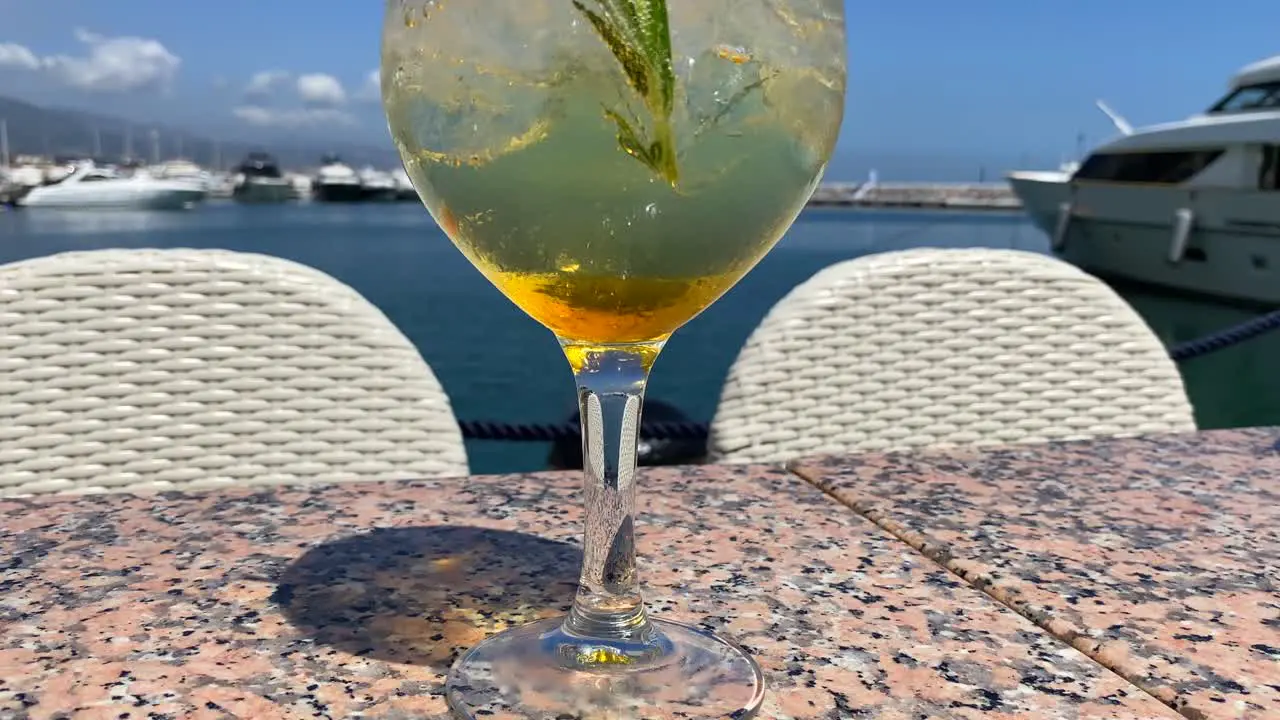 Fancy cocktail with champagne and rosemary by the sea in Puerto Banus with yachts luxury holiday destination drink on a tropical vacation with sea view in Marbella Spain 4K shot