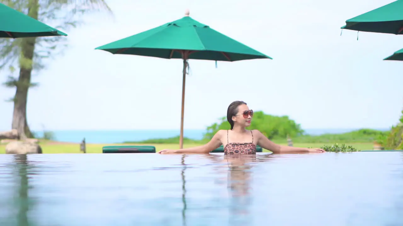 Asian woman sitting in pool with tropical background