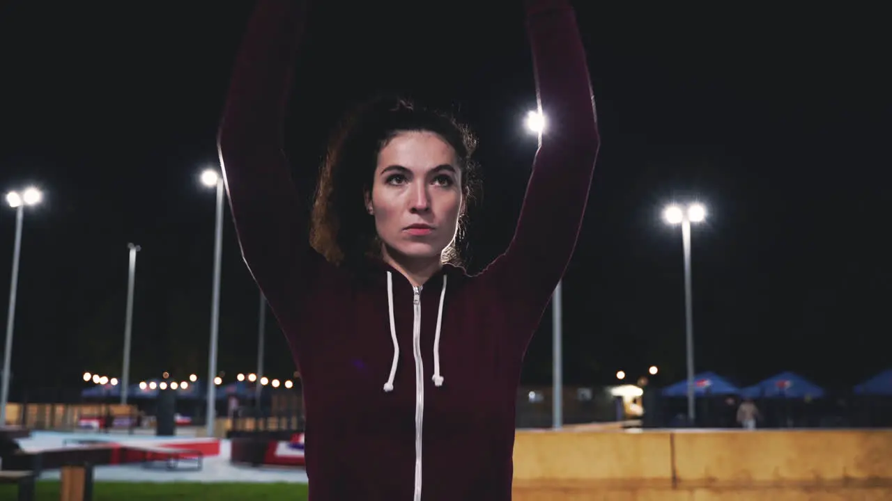 Chica Rizada Deportiva Estirando Y Girando Los Brazos En El Parque Por La Noche 3