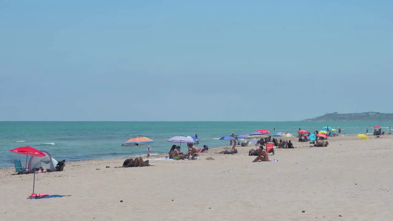 People sunbathe while sitting at the beach on the shore of the Mediterranean sea in Alicante Spain