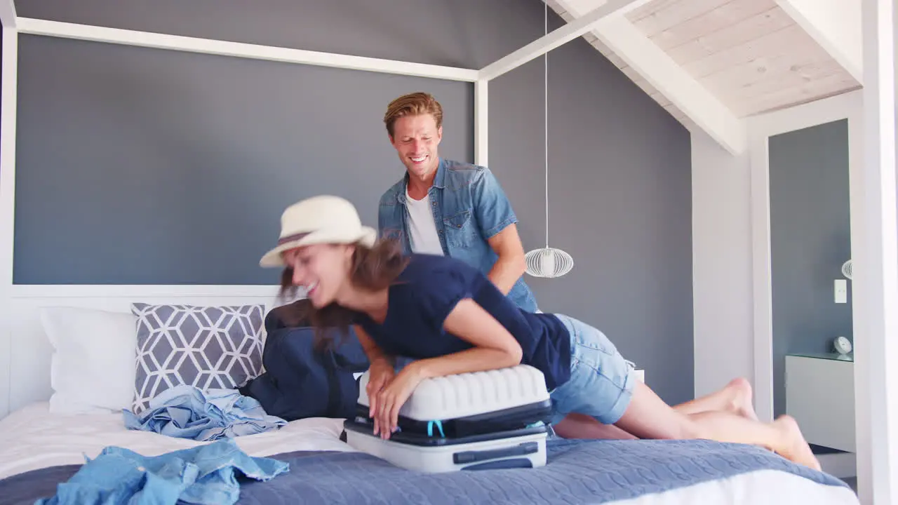 Couple Trying To Close Full Holiday Suitcase In Bedroom