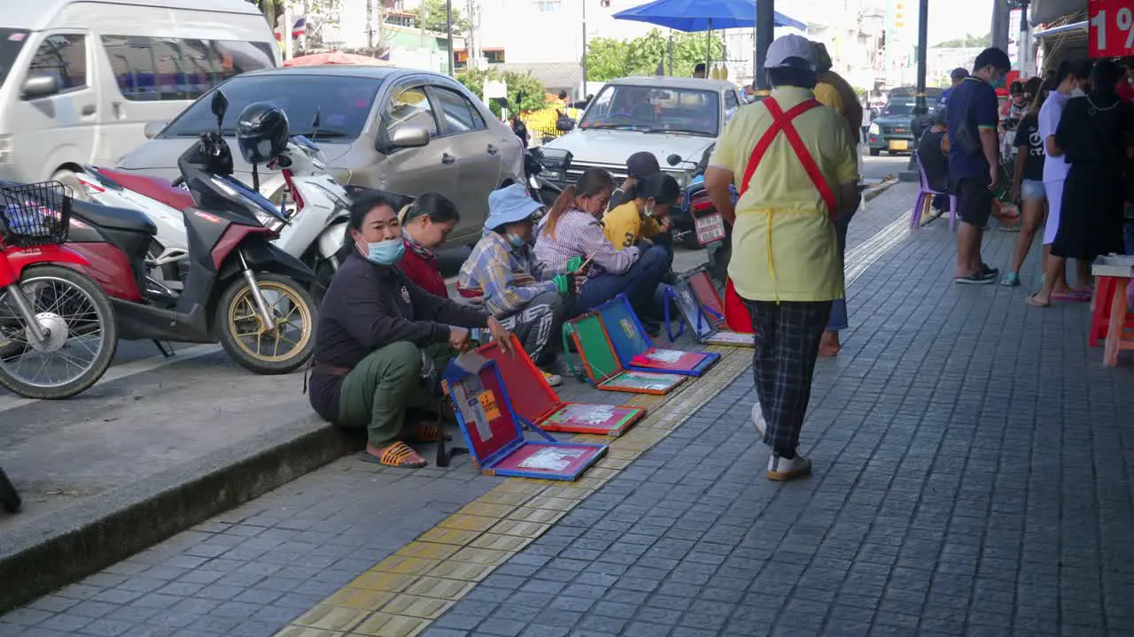 Shot of a group of ladies sitting on the pavement selling lottery tickets along the roadside in Songkhla Province Thailand at daytime