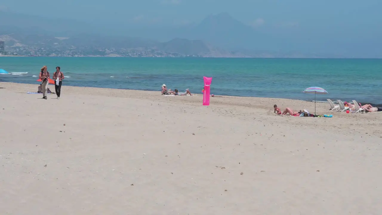 People sunbathe while lying down at the beach on the shore of the Mediterranean sea in Alicante Spain