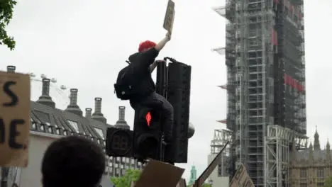 London Black Lives Matter Protester Sitting Above Crowds On Traffic Light