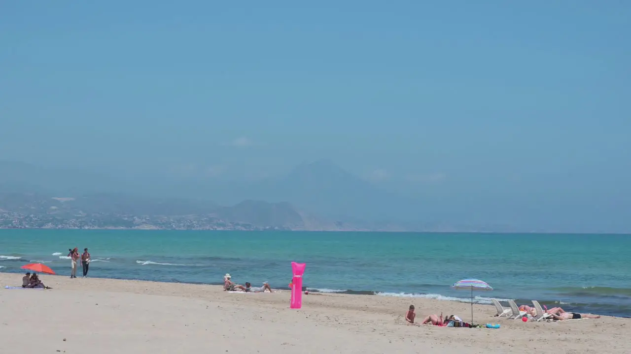 People sunbathe while lying down and have a stroll at the beach on the shore of the Mediterranean sea in Alicante Spain