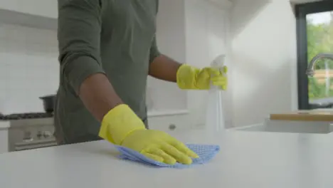 Man Cleaning Kitchen Surface with Rubber Gloves and Disinfectant Spray