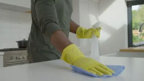 Man Cleaning Kitchen Work Surface with Rubber Gloves and Disinfectant Spray