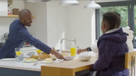 Father Hands Bowl of Raspberries to Two Young Children at Breakfast