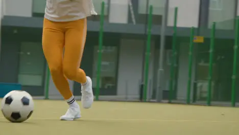 Close Up Of Woman On Artificial Soccer Pitch In Urban City Area Shooting At Goal With Football 