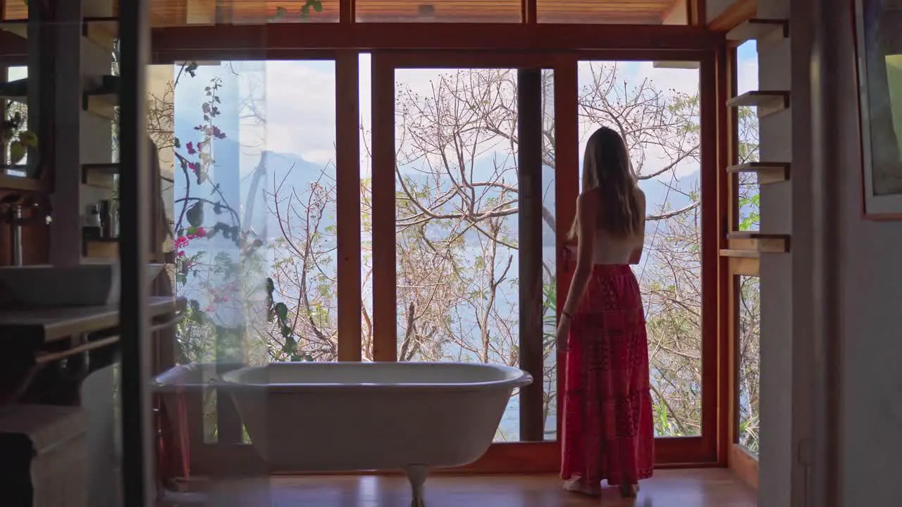 Girl on holiday entering bathroom and opening window to lake and volcano views in Lake Atitlan Guatemala