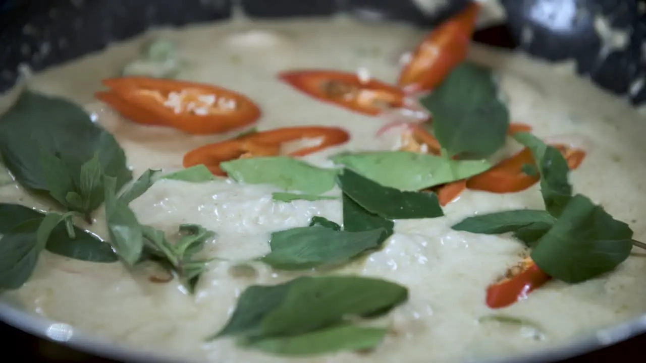 Garnishing Boiling Green Curry with Red Chili and Green Thai Basil Close Up