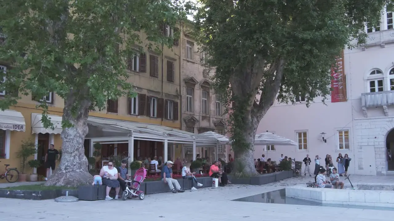 Life at its best catching a bit of the traditional way in Dalmatian town of Zadar Croatia with people sitting in the shade of trees and talking Five Wells square Croatia