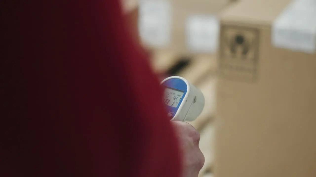 Over the shoulder of medical thermometer gun with defocused boxes in background