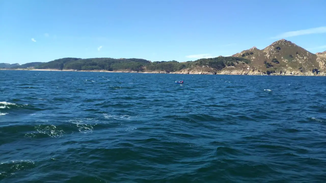 Boat with fishermen sailing fast the sea altered near the Cíes Islands in the Rías Baixas sunny day of blue sky in the Rías Baixas shot traveling laterally to the left Pontevedra Galicia Spain