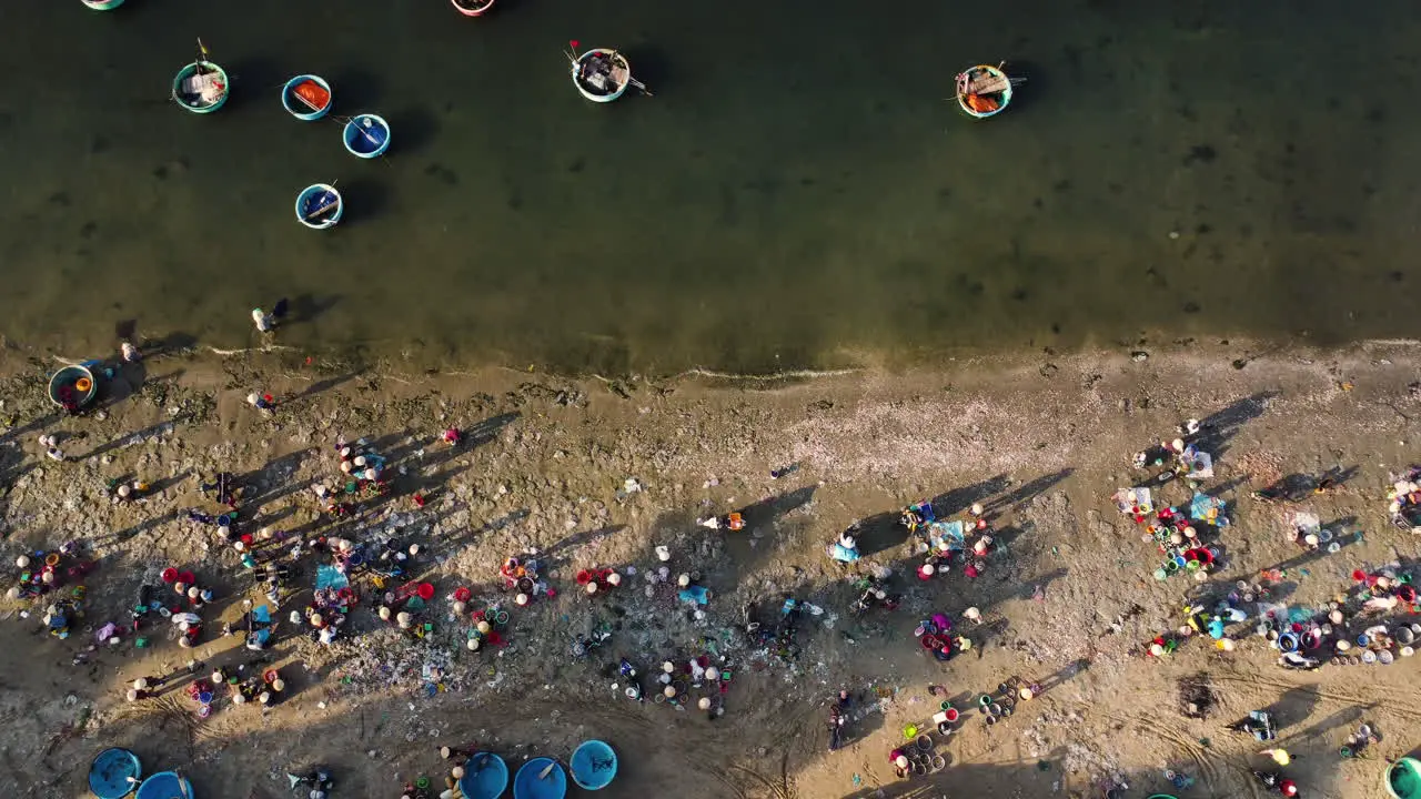 Aerial top down Vietnamese fishing villagers crowded on beach shore