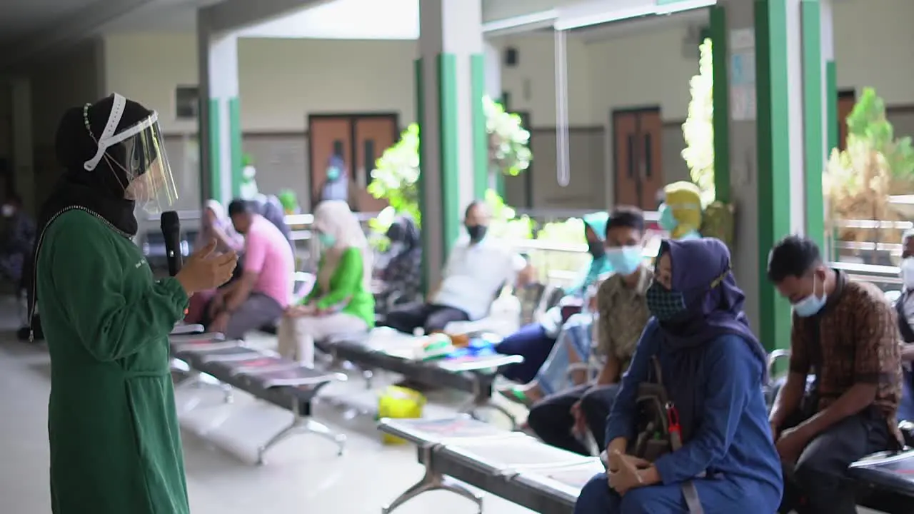 A group of Asian seniors sit in a row in a hospital pavilion and listen to a nurse during a therapy session