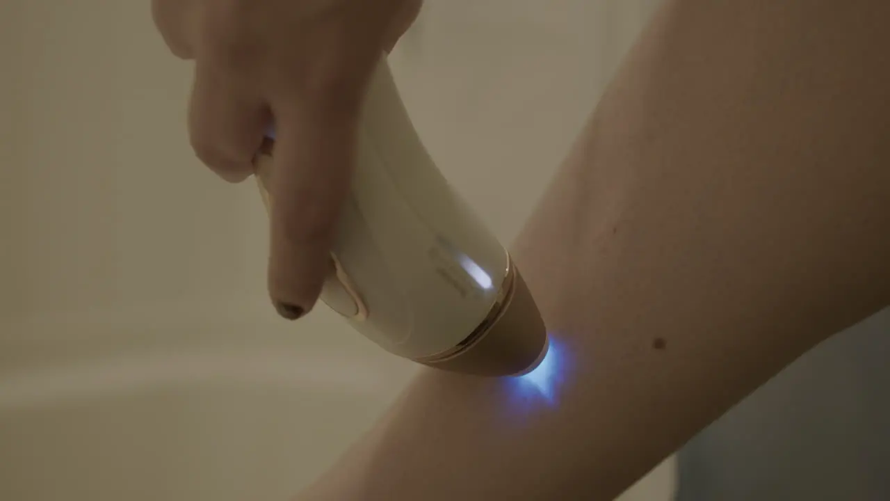 Close Up Slow Motion of a Woman Using an Intense Pulsed Light Hair Removal Device on Her Leg