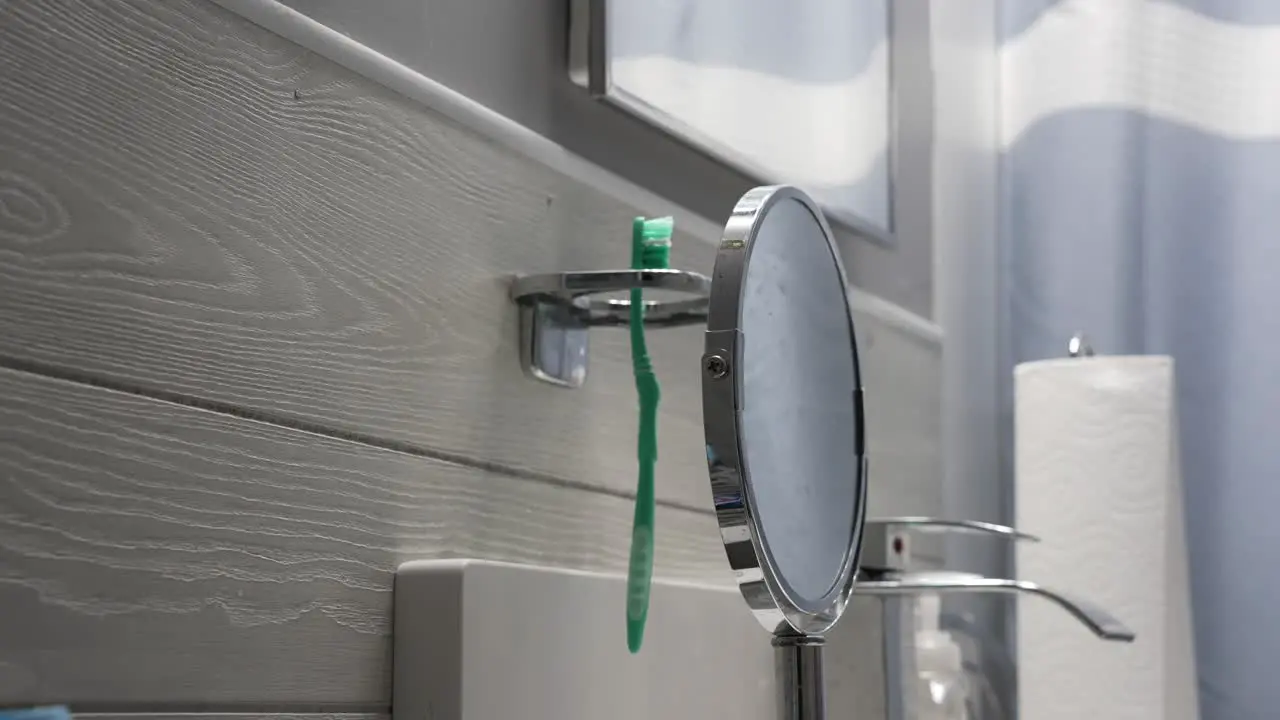 Man puts away his green toothbrush in a grey bathroom