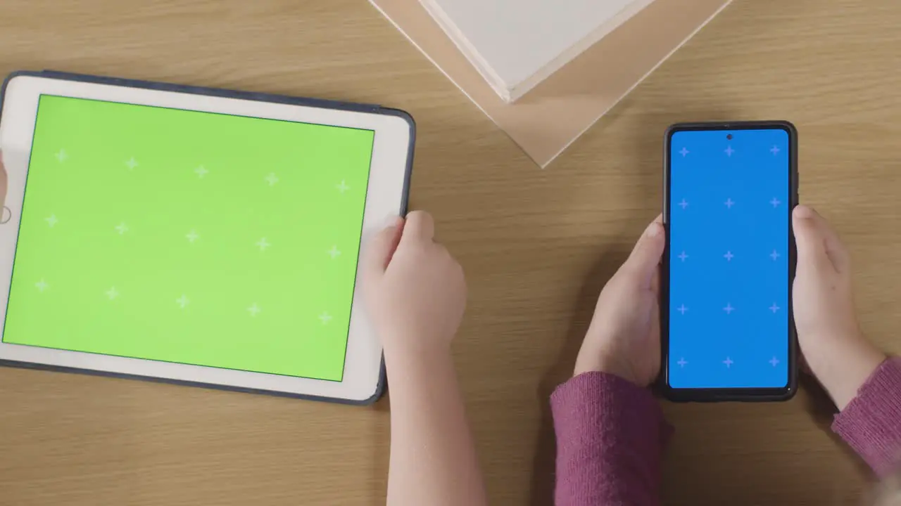 Overhead Shot Of Children Using Green Screen Digital Tablet And Blue Screen Mobile Phone On Table At Home 2