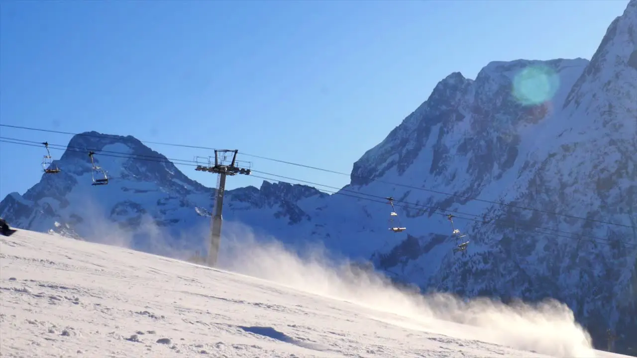 unrecognizable skier and snowboarder passing by the camera in slow motion spraying smoke clouds with beautiful mountain backdrop going down a steep black piste