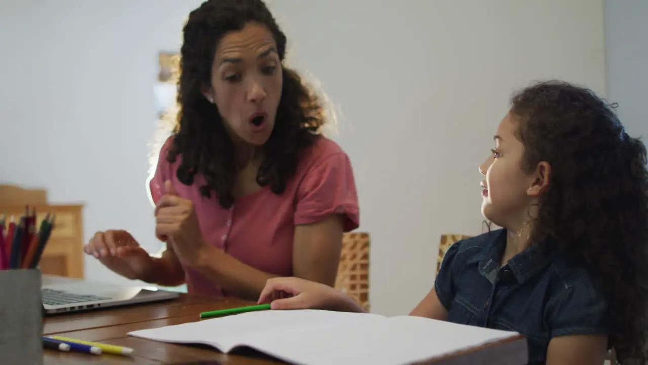 Happy mixed race mother and daughter doing homework together at home