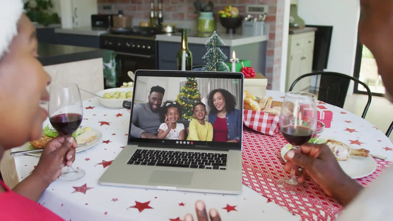 African american couple with wine using laptop for christmas video call with happy family on screen