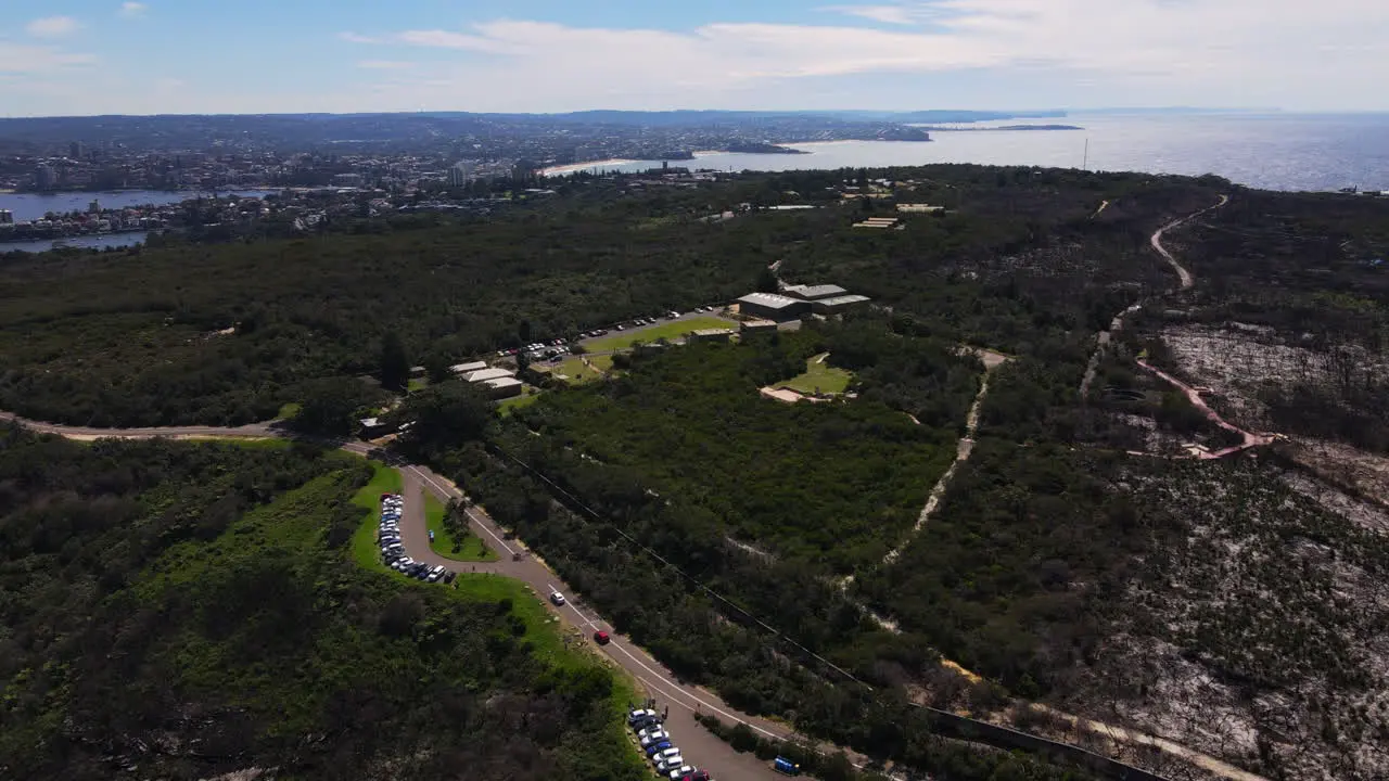 High Drone shot over dense park bushland with Sea and suburbs in the background headland in Australia