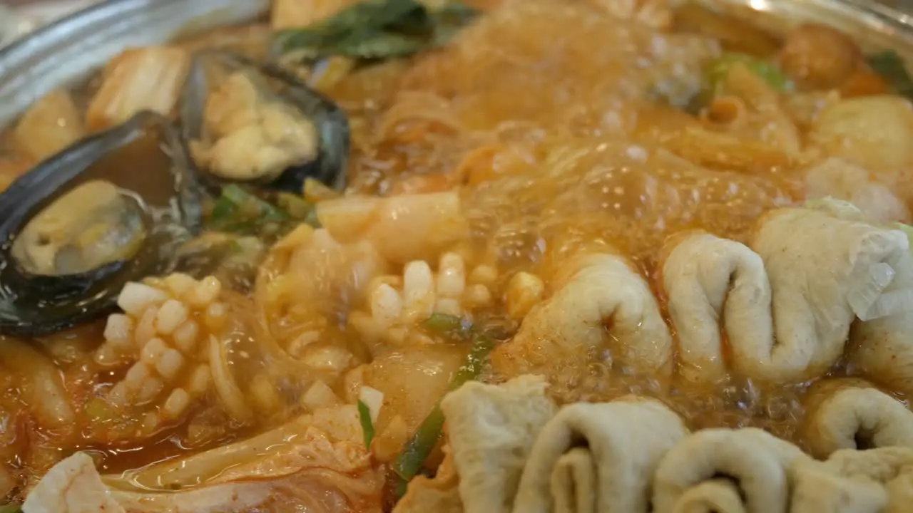 close up to boiling Korean Kimchi tteok pokki soup full with pork squid mussles ehmook fish plate and vegetable