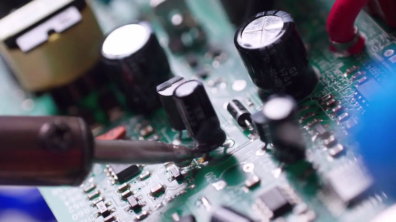 Close-up of a technician soldering a capacitor to a circuit board with a wisp of smoky fumes coming out of it