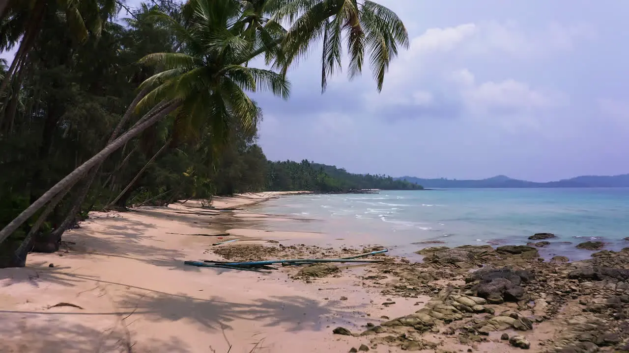 Palm trees along white sand beach washed by ocean waves Koh Kood