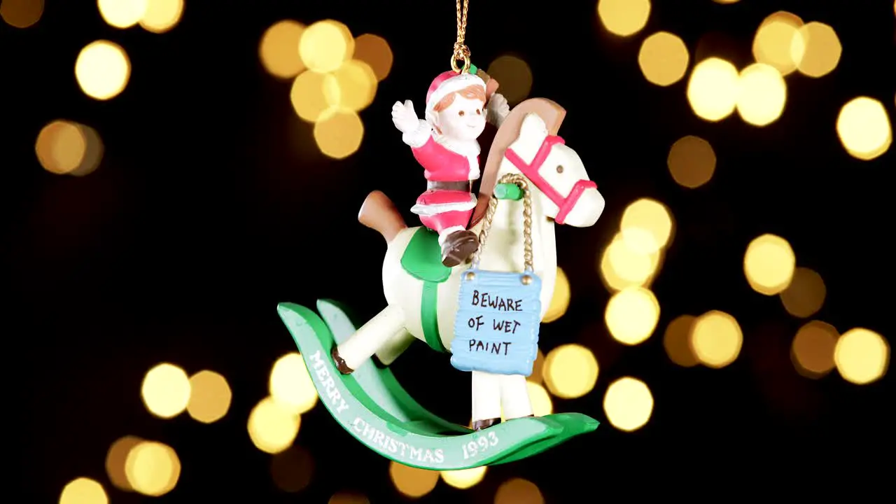 single wooden Christmas ornament of a boy on a rocking horse with out of focus lights flickering in the background close up