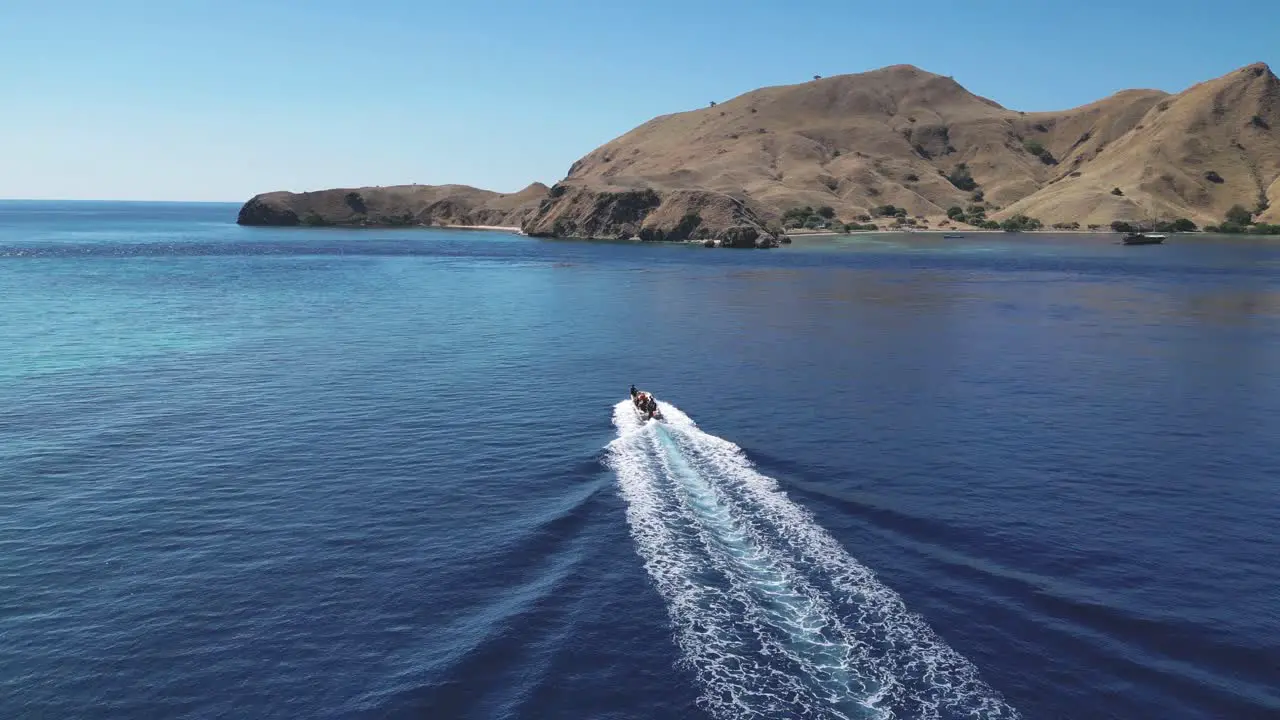 Drone following and descending over a speedboat racing towards a dry and barren island