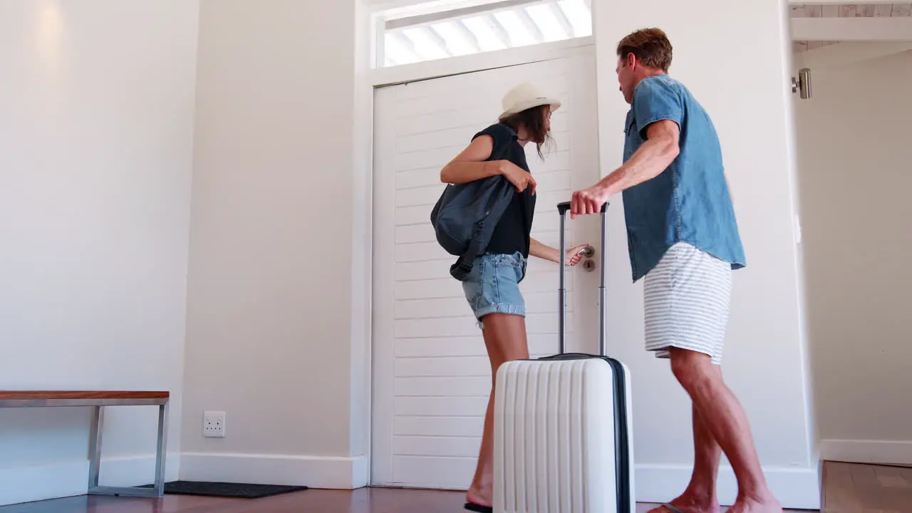 Rear View Of Couple With Luggage Leaving Home For Vacation