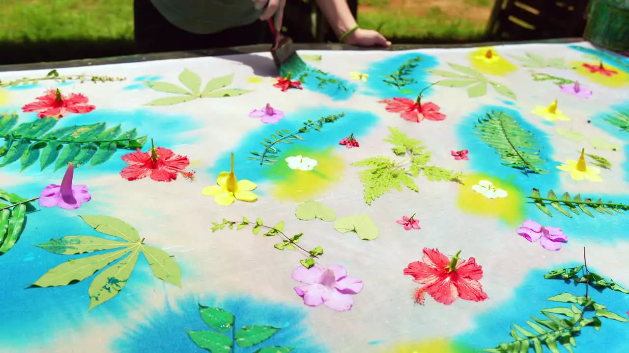 Clients learning homemade batik sarong pareo placing blue paint on leaves on white cloth Mahe Seychelles 25fps 4