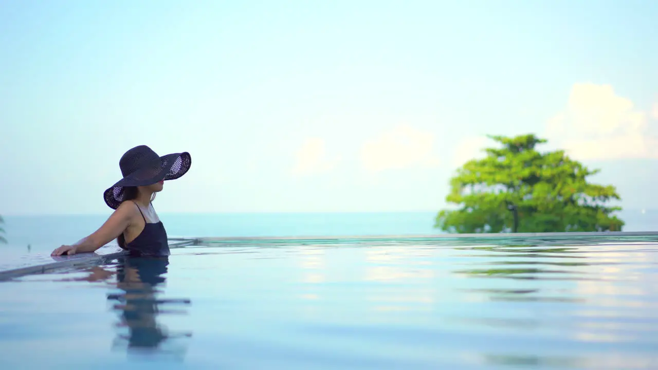 Beautiful elegant woman in fashionable swimwear in infinity pool blurred background soft light