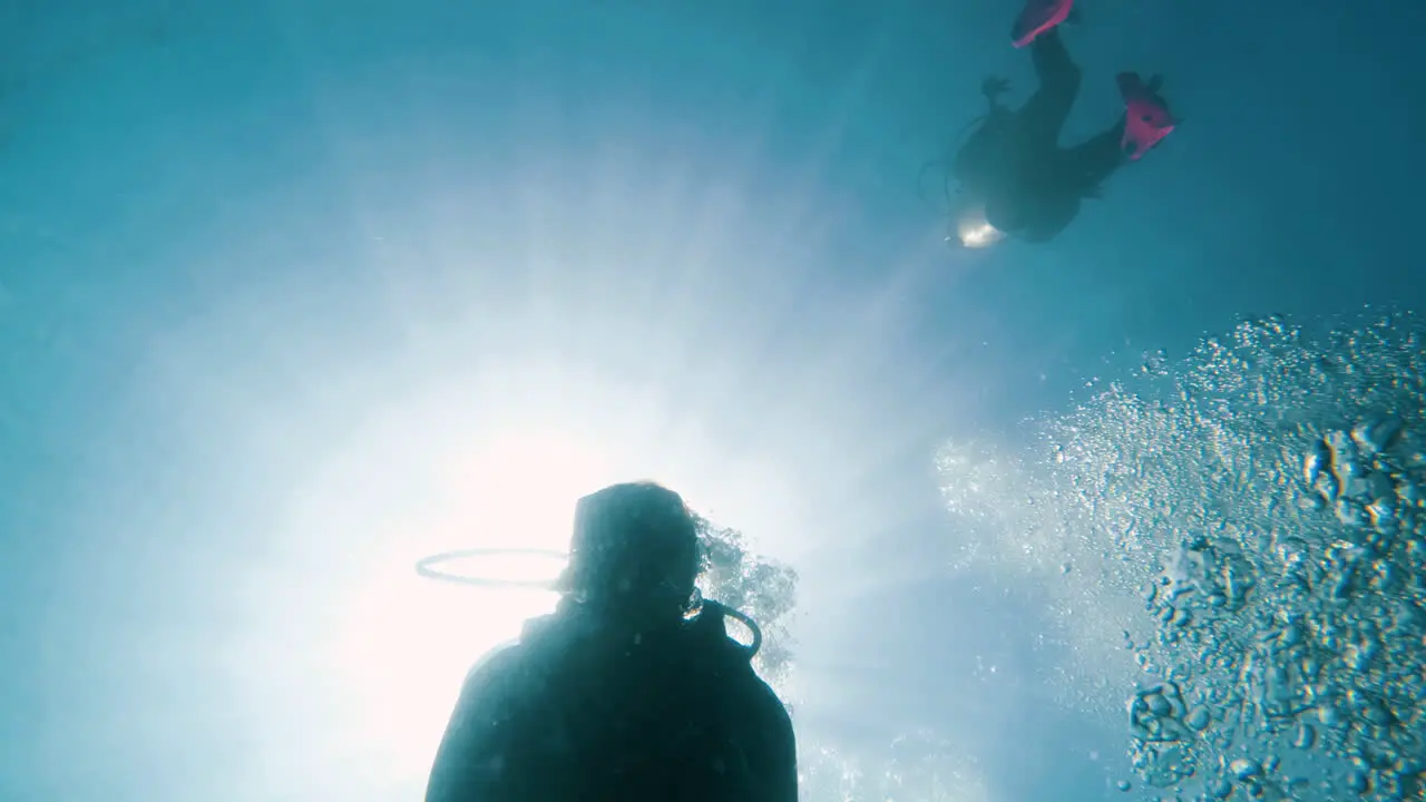 Cinematic slow motion shot of scuba diver filmed from below with the sun from above and bubbles in the frame 120FPS Slomo