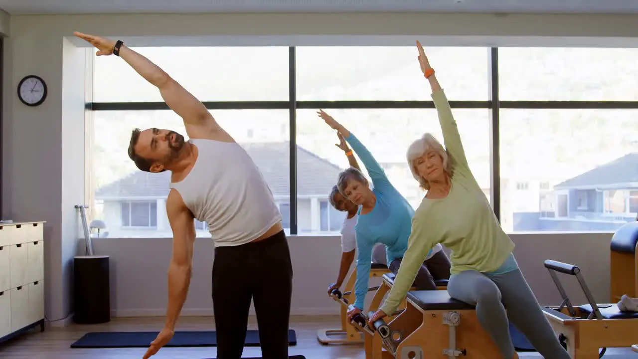 Trainer assisting senior women in performing yoga 4k