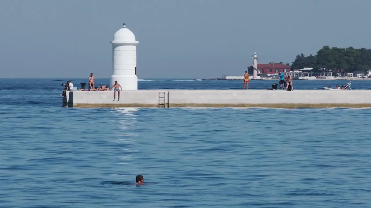 People sun bathing at Zadar promenade with beacon and distant lighthouse Croatia summer