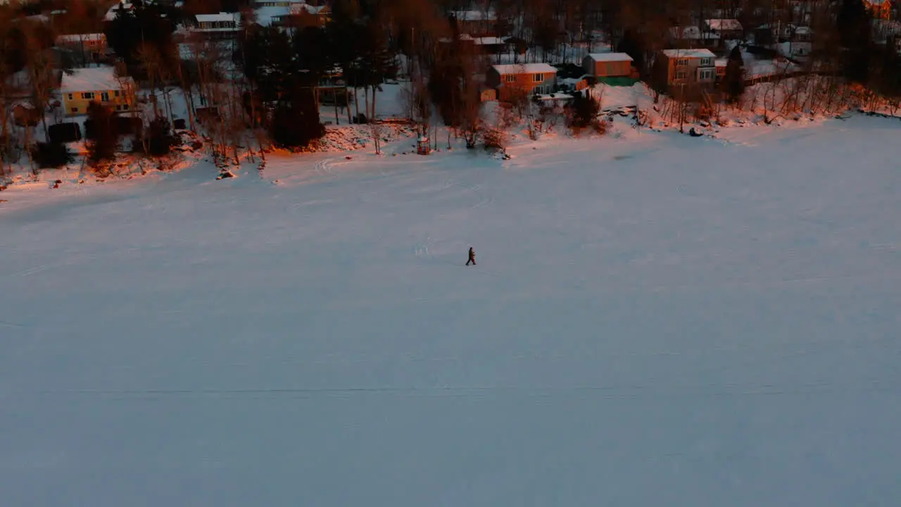 Aerial view of a person snowshoeing along a frozen river at sunset