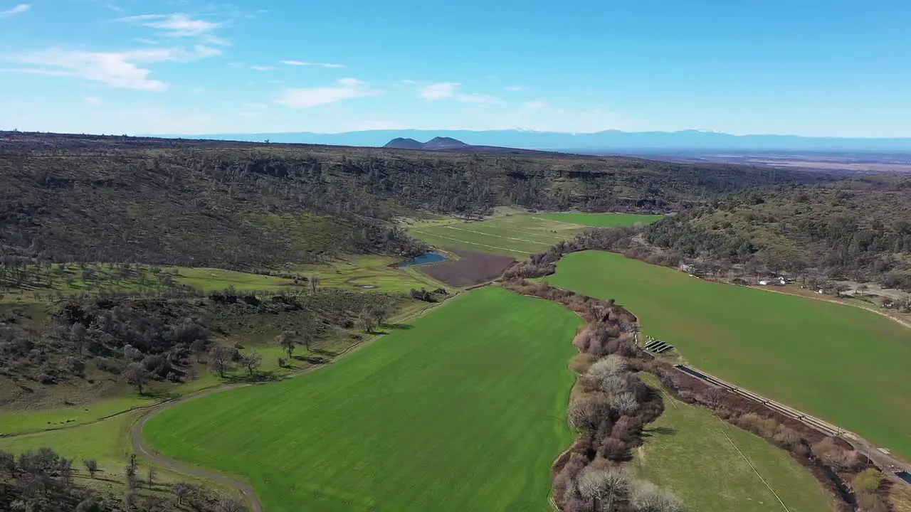 600' drone flyover of green valley lined with mountains and a creek lined with trees running through the middle of it