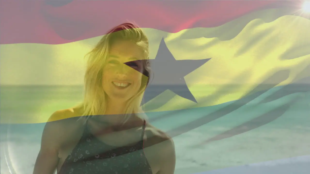 Animation of waving flag of ghana over smiling caucasian woman standing against sea at beach