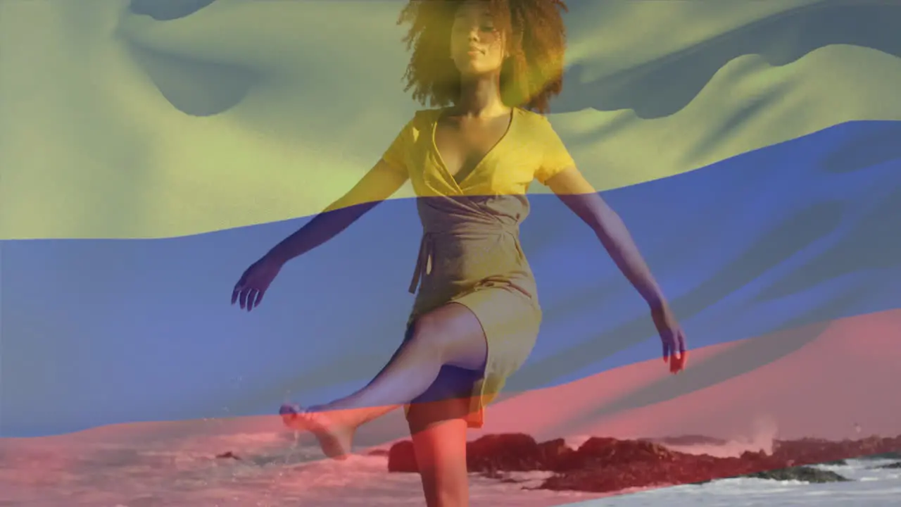 Animation of flag of colombia waving over biracial woman walking and enjoying breeze at beach