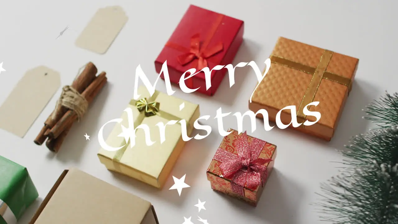 Animation of merry christmas text and stars overhead view of multicolored gift boxes on table