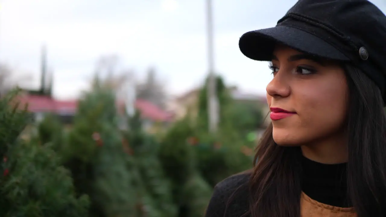 A hispanic woman shopping on a Christmas tree lot with green fir conifers in a seasonal holiday nursery