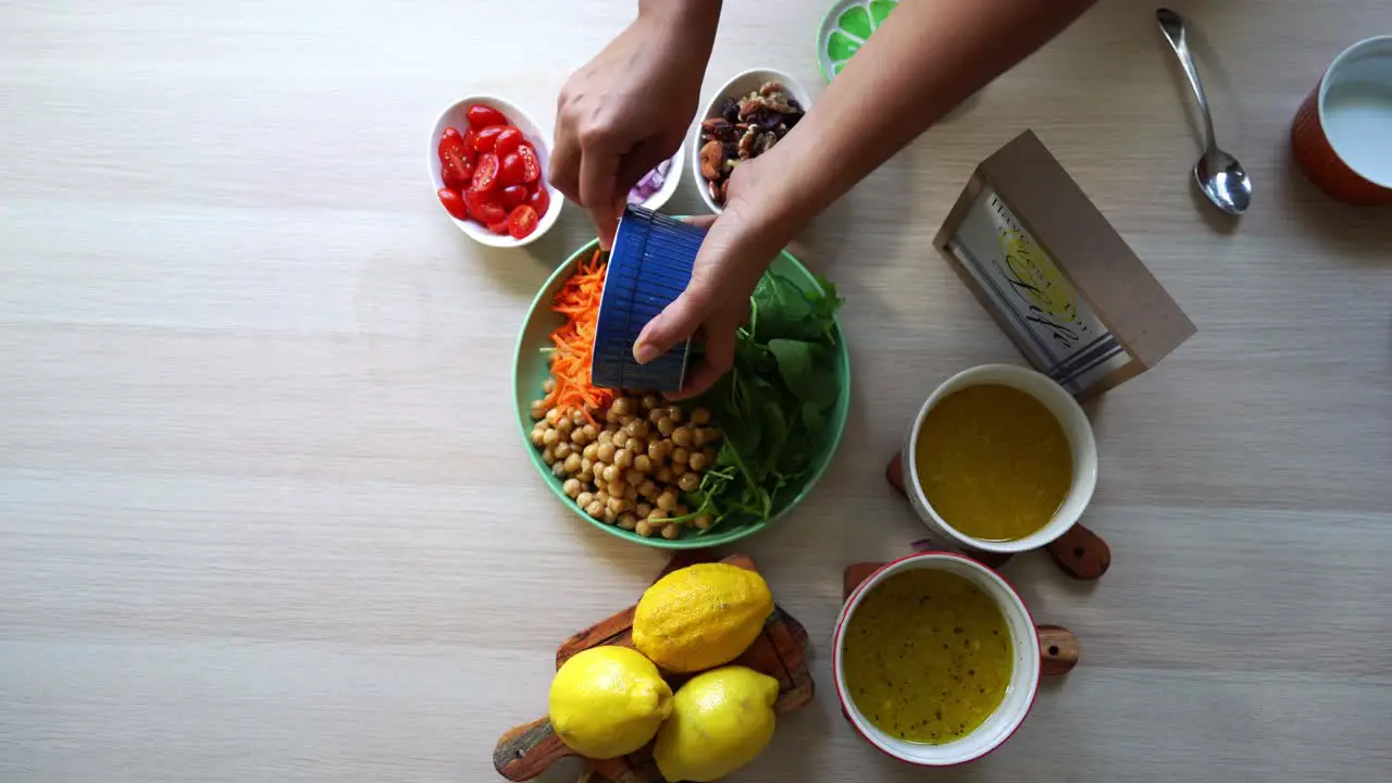 Aerial shot making of a salad adding chick peas tomatoes carrots spinach chick peas lemons onions nuts dressing in view