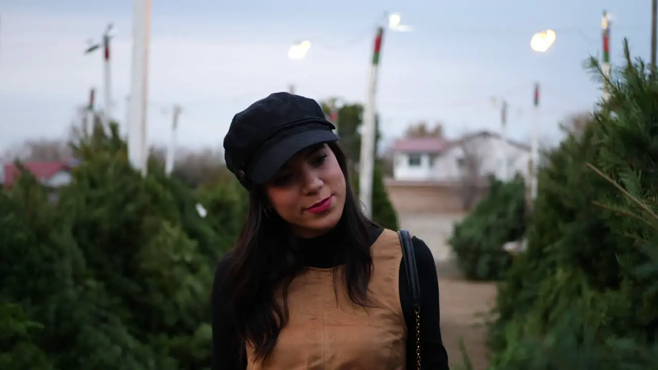 A hispanic woman shopping for a season holiday Christmas tree on a lot with many species of fir trees