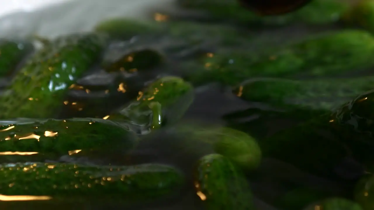 Cucumbers float in a bowl full of water they are stirred with a spoon