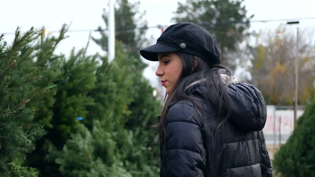 A hispanic woman shopping for a seasonal holiday Christmas tree decoration on a lot with many species of festive trees