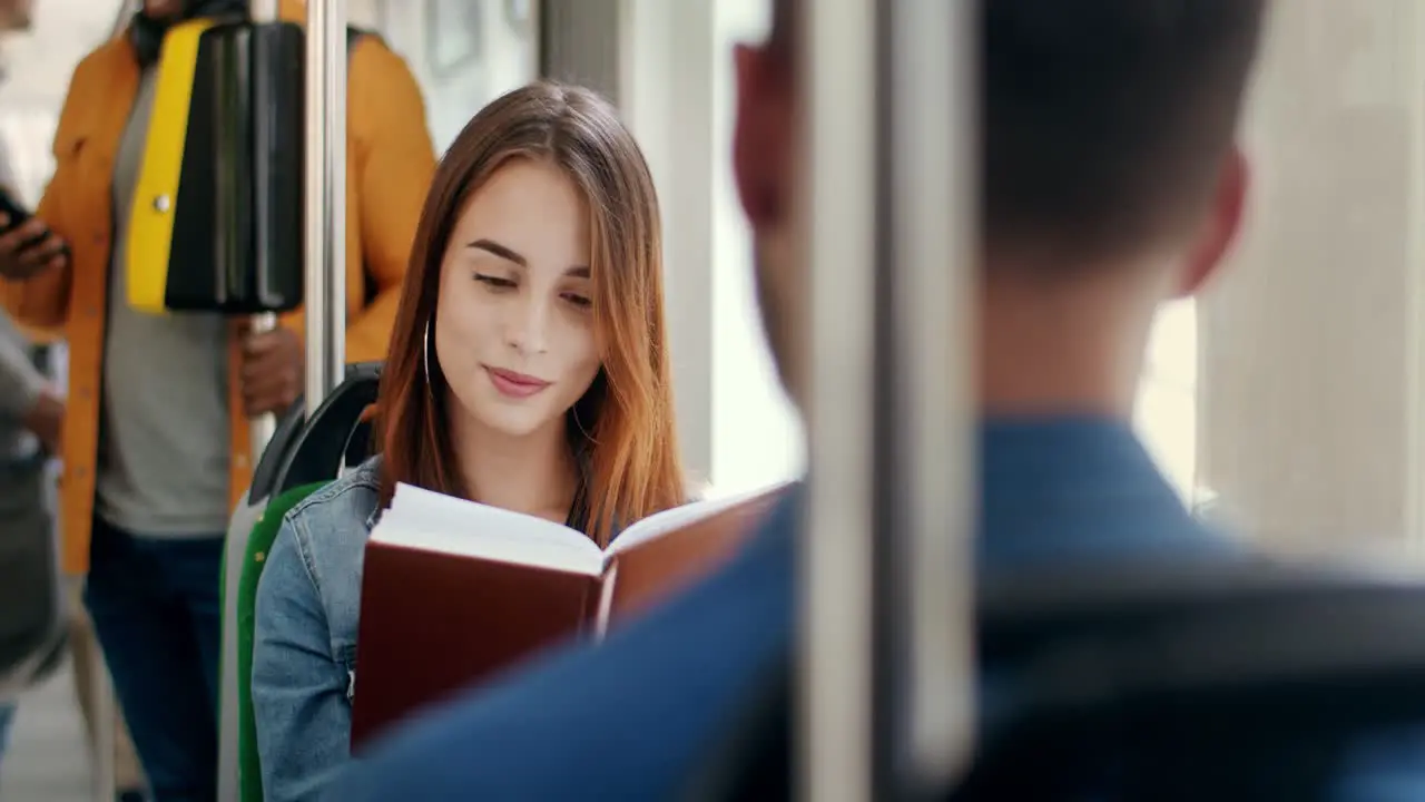 Young Beautiful And Happy Girl Reading A Book In The Tram And Smiling Then Flirting With A Young Handsome Man Who Sitting In Front Of Him