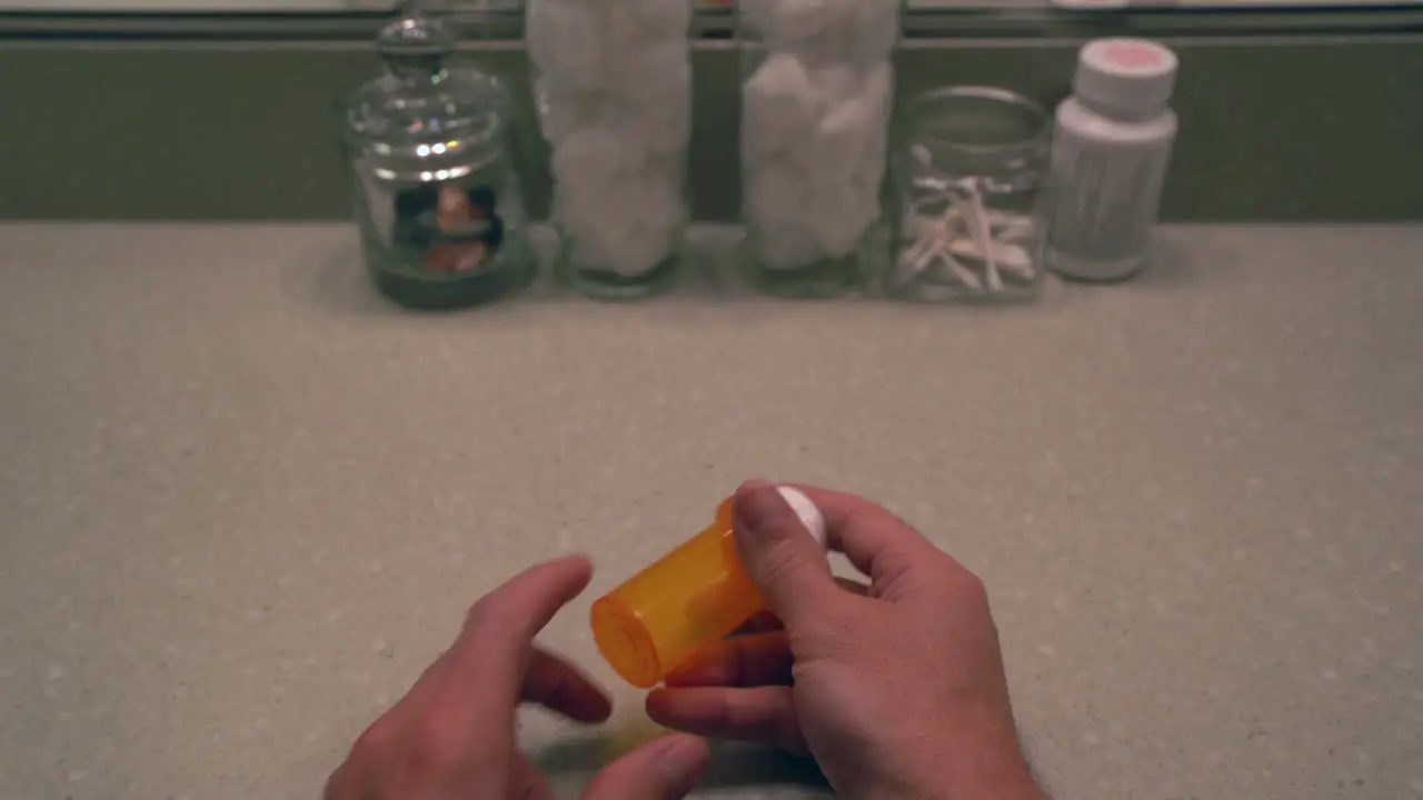 Man opening a pill bottle and taking opioid at his bathroom vanity 1